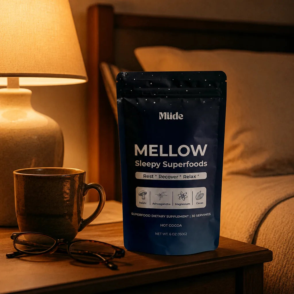 Mellow pouch on a bedroom nightstand beside a lit lamp, a warm mug and folded reading glasses