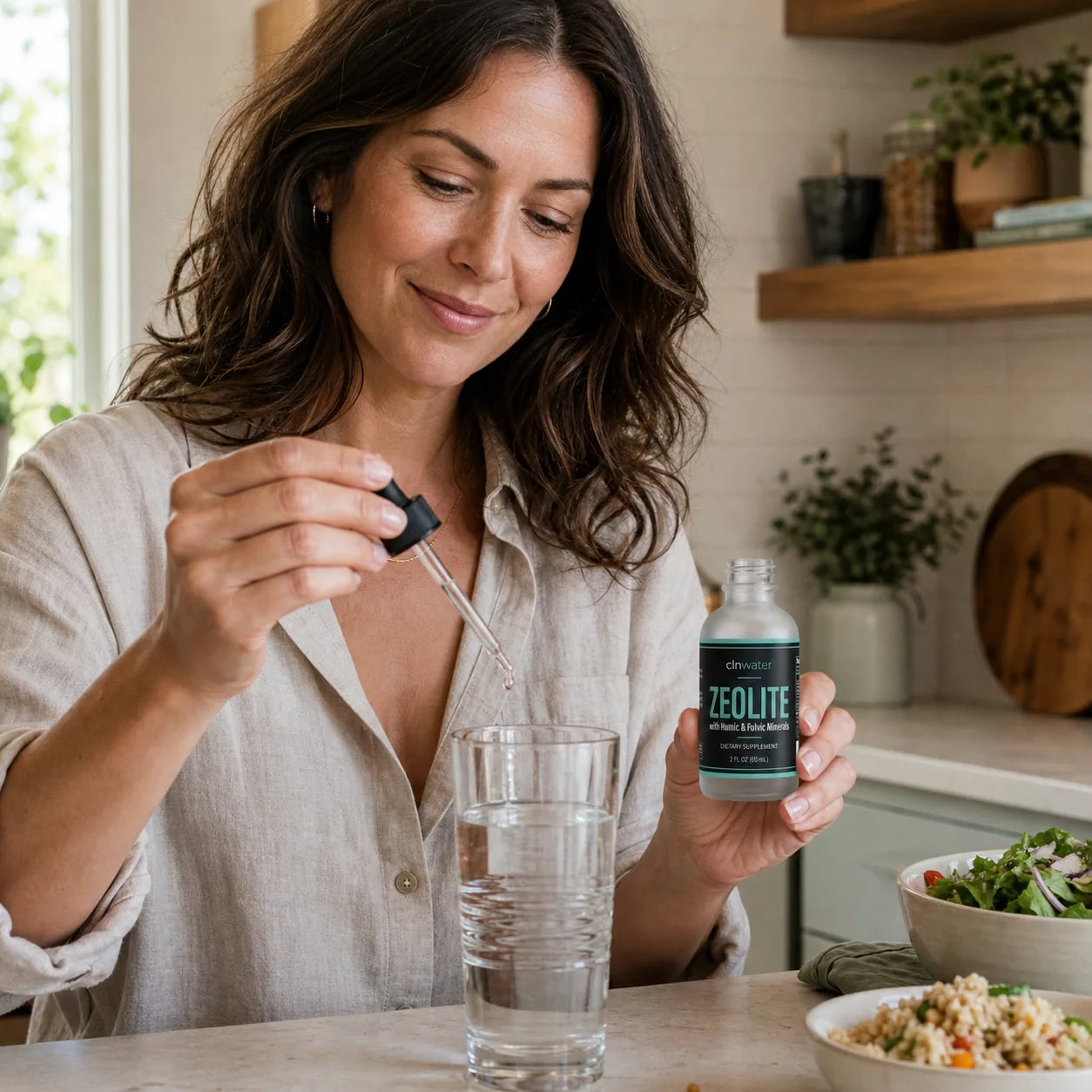Healthy woman adding Trace drops to a glass of water beside lunch