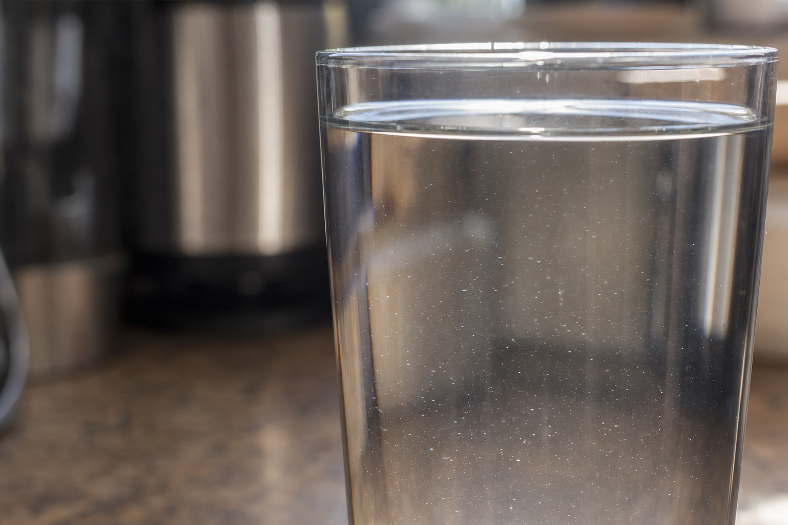 A glass of tap water with barely visible suspended particles.