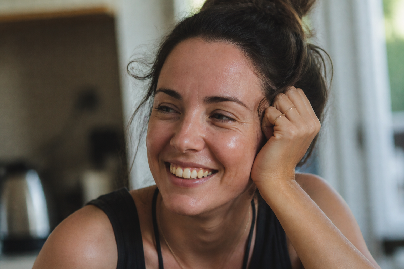 A woman smiling openly in natural window light